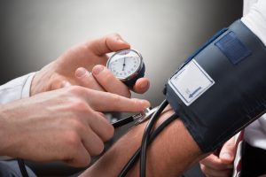 A doctor is taking a patient's blood pressure reading as part of a discussion of the patient's risk factors for heart disease, which include high blood pressure, high cholesterol, diabetes, and unhealthy diet.